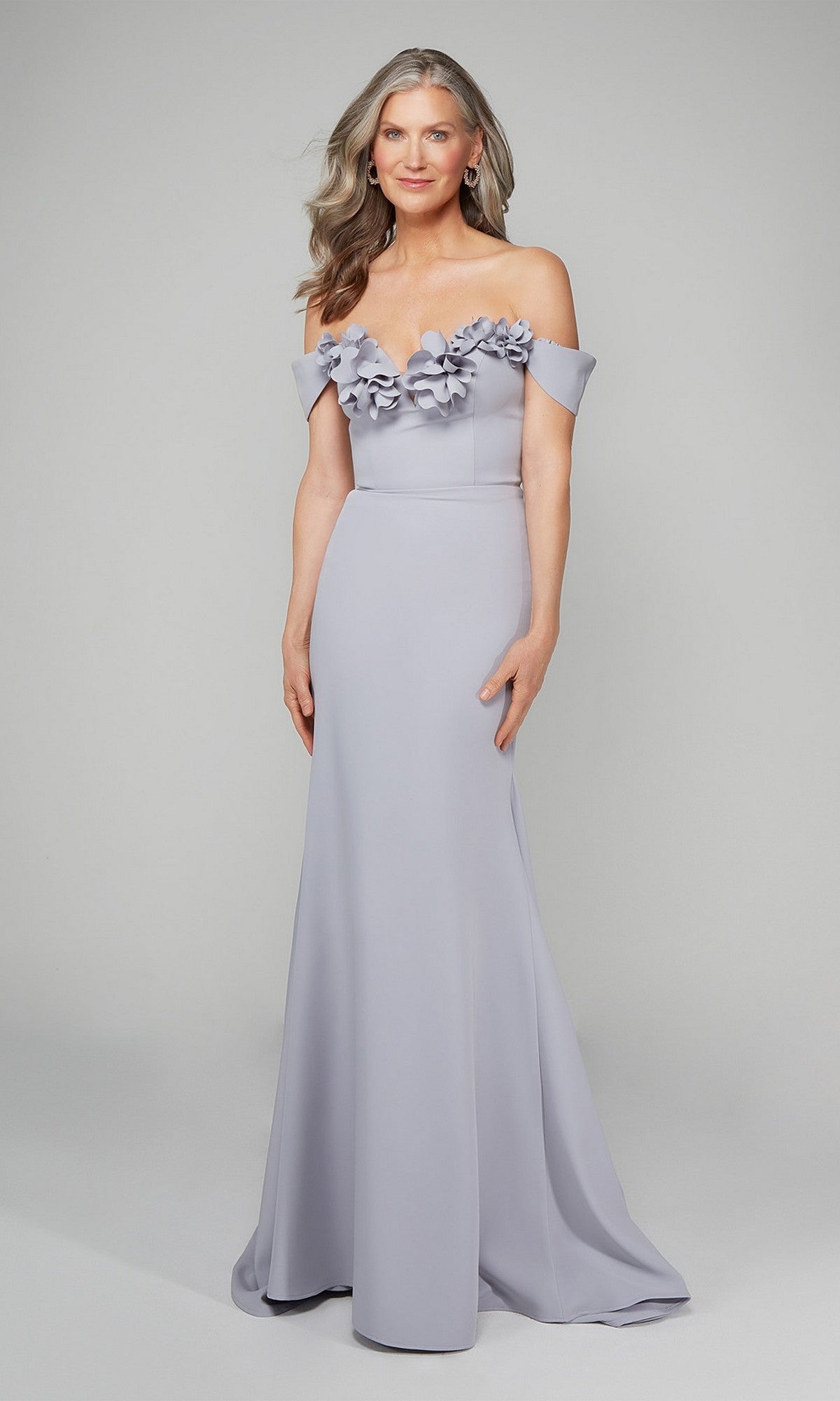 A woman models the Alyce 7062 long formal dress in light lavender, detailed with 3D floral accents on the off-the-shoulder neckline, against a plain background—an elegant choice for evening occasions.